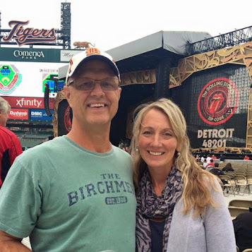 A middle-aged couple pose together for a photo in front of the stage at a Rolling Stones concert in Detroit. It appears the concert is at Comerica Park, home of the Detroit Tigers baseball team. 